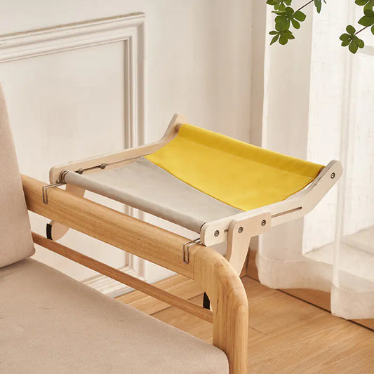 Yellow pet bed attached to a wooden frame on a couch with a white curtain in the background.