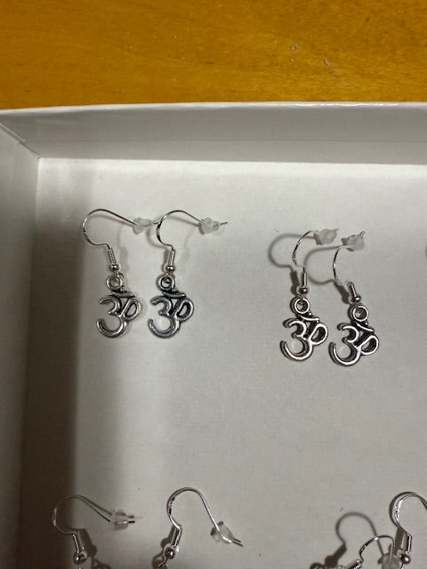 Silver earrings on a white surface with OM symbol and a wooden background