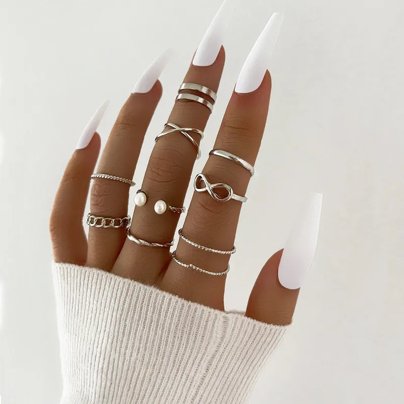 Hand wearing multiple silver rings with a plain background