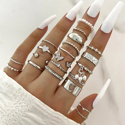 Hand wearing multiple silver rings with various designs on a neutral background