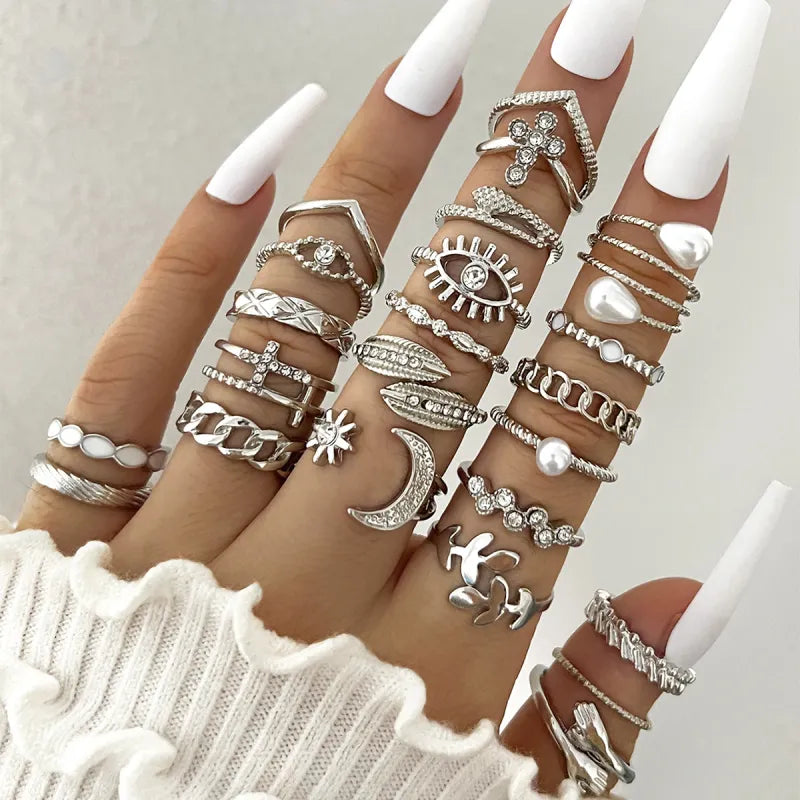 Multiple silver rings with various designs on a hand with white nail polish.