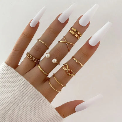 Hand wearing multiple gold rings with white nail polish on a neutral background