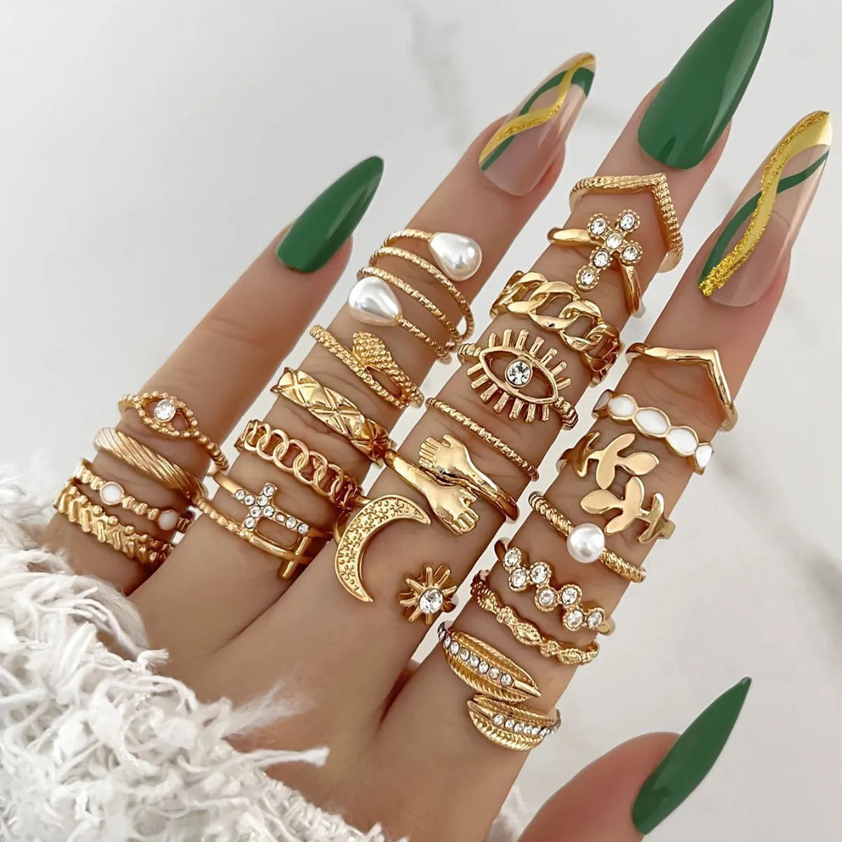 Hand wearing multiple gold rings with green nail polish on a white background