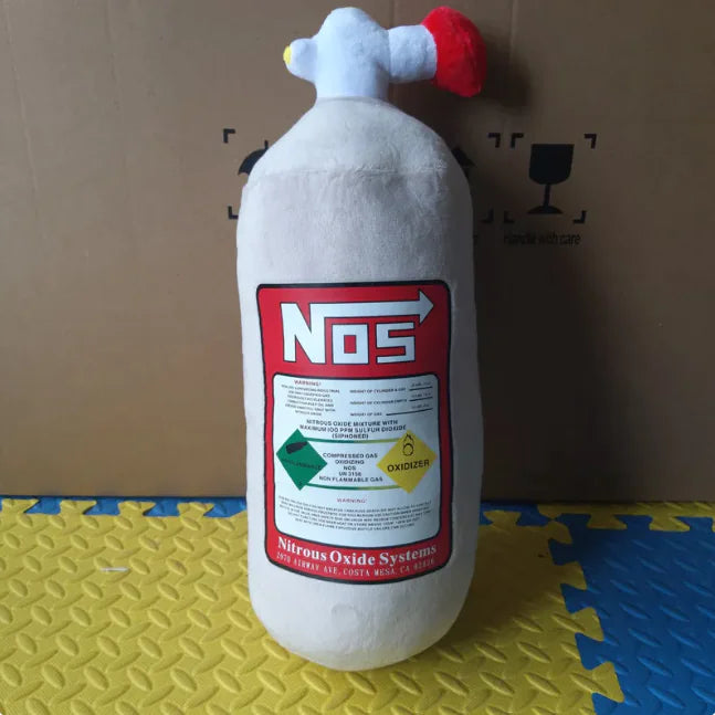 Plush toy shaped like a NOS bottle on a yellow and blue mat with a cardboard box in the background.