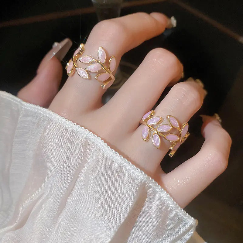 Hand wearing two decorative rings with pink leaves on a blurred background