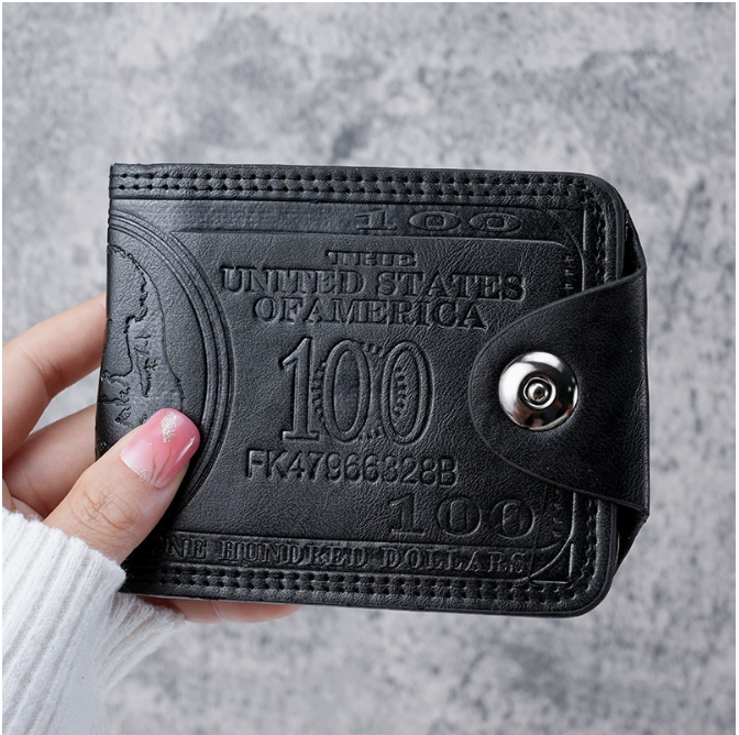 Black wallet with embossed design held by a hand against a gray background